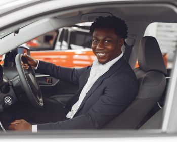 Man buying the car. Businessman in a car salon. Black male in a suit.