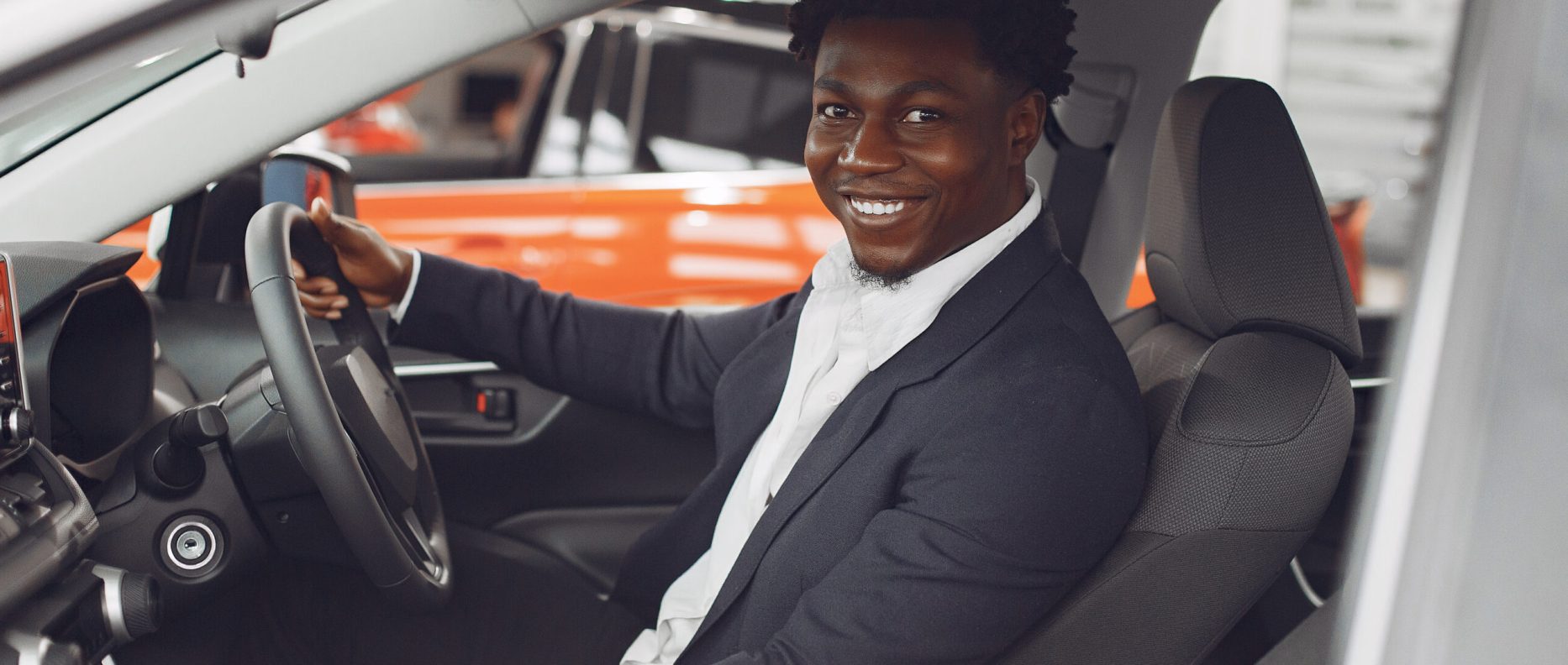 Man buying the car. Businessman in a car salon. Black male in a suit.